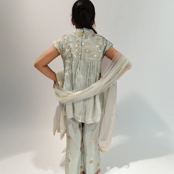 Girl wearing a light green traditional outfit with a floral pattern on a white background