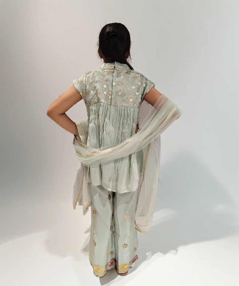 Girl wearing a light green traditional outfit with a floral pattern on a white background