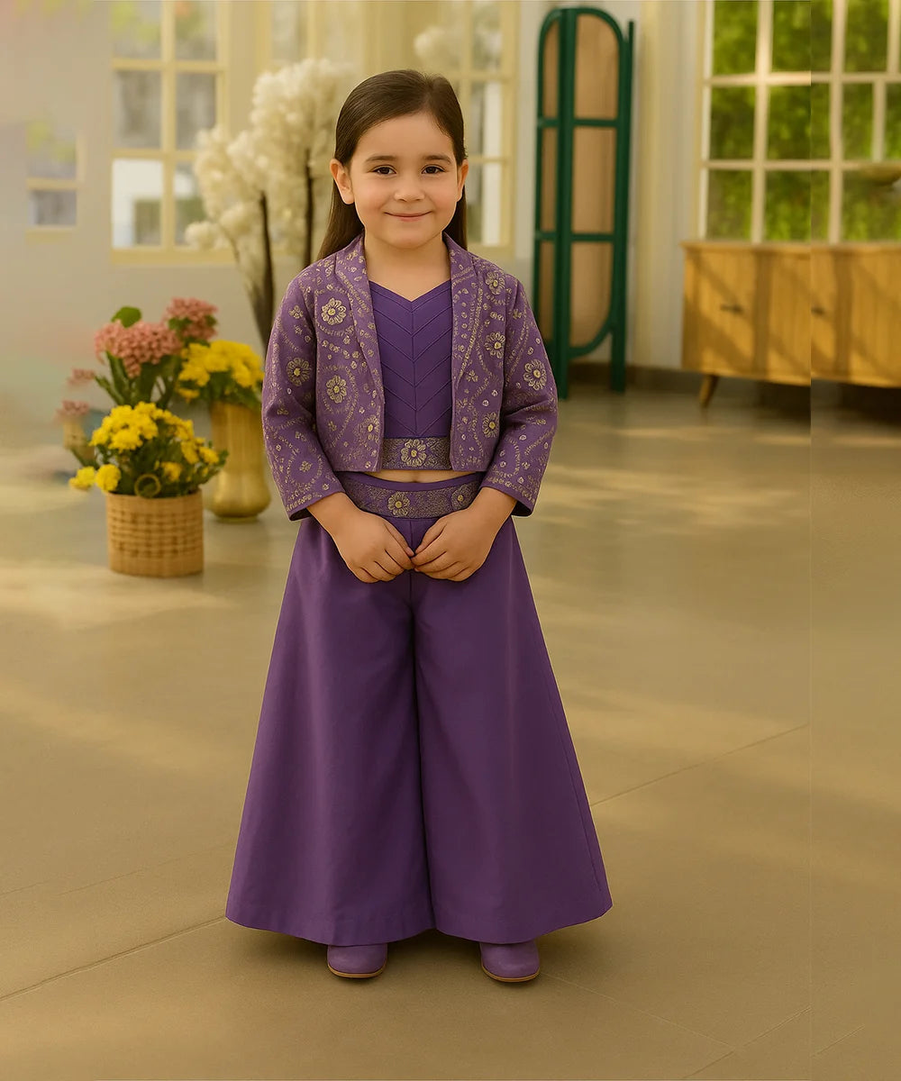 Young girl in a purple traditional outfit standing indoors with flowers in the background