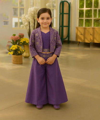 Young girl in a purple traditional outfit standing indoors with flowers in the background