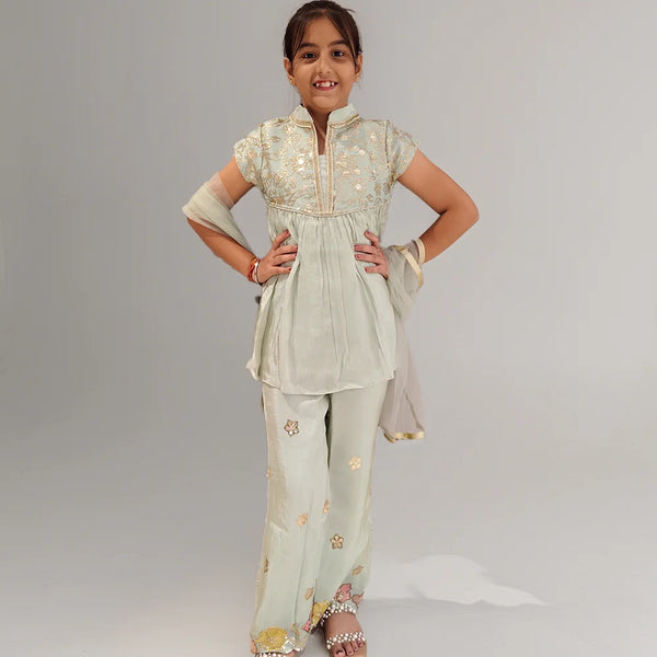 Young girl wearing a light green traditional outfit with floral patterns on a plain background