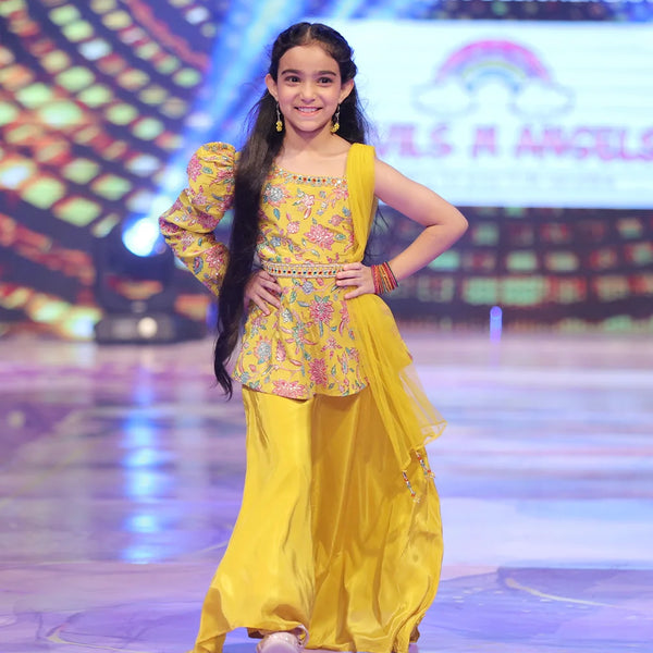 Young girl in a yellow sharara traditional outfit on a stage with colorful background