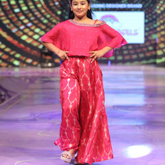 Young girl in a pink sharara outfit on a stage with a colorful background