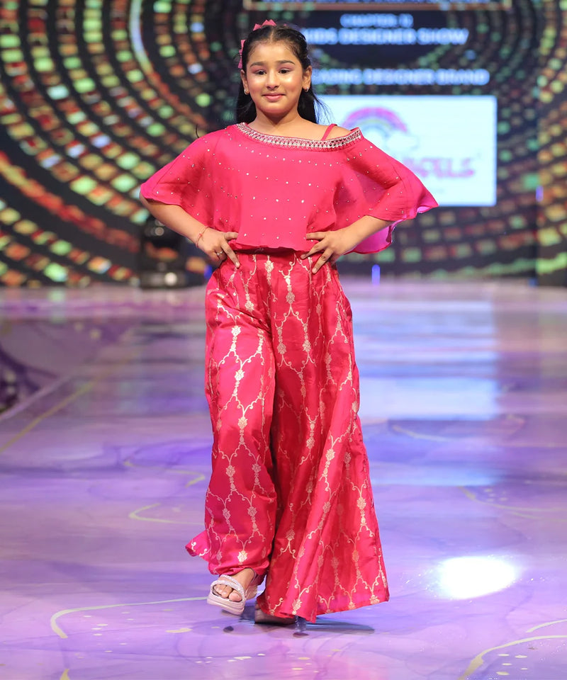 Young girl in a pink sharara outfit on a stage with a colorful background