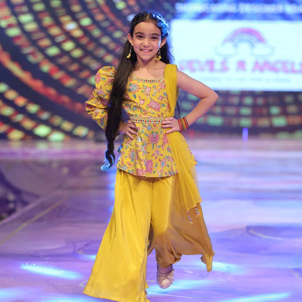 Girl in a yellow sharara traditional outfit on a stage with colorful background