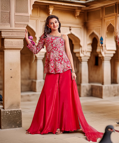 Woman in a red and pink traditional outfit standing in an architectural setting.