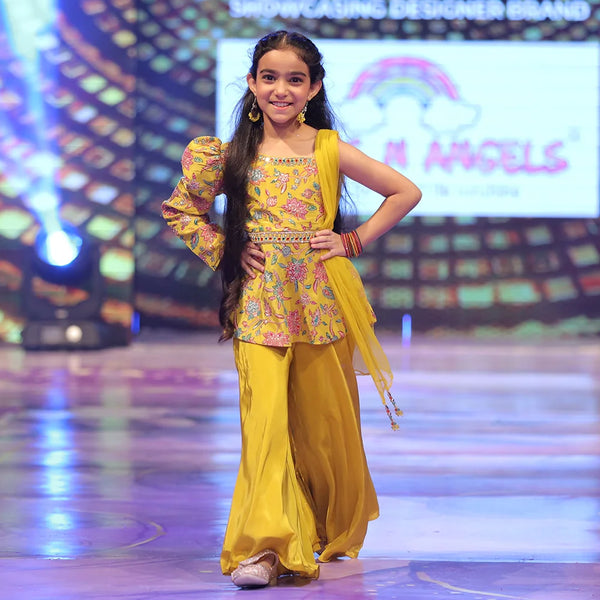 Young girl in a yellow sharara outfit on a stage with colorful background