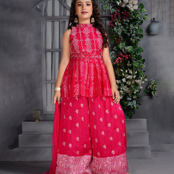Young girl wearing a pink traditional outfit with white patterns in a decorative setting.