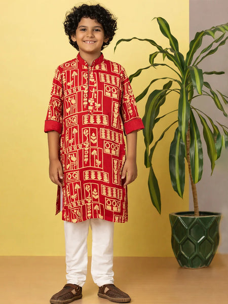 Child wearing a red traditional outfit with white patterns, standing next to a potted plant against a yellow wall.