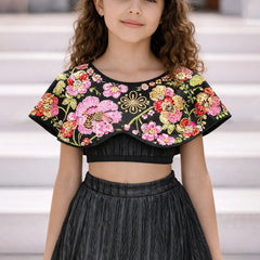 Young girl wearing a black top with colorful floral embroidery and a black skirt.
