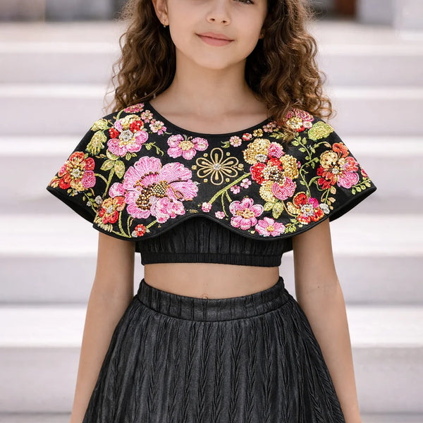 Young girl wearing a black top with colorful floral embroidery and a black skirt.