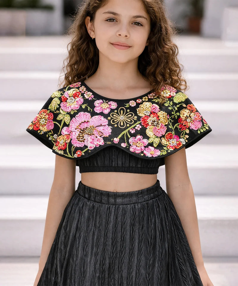 Young girl wearing a black top with colorful floral embroidery and a black skirt.