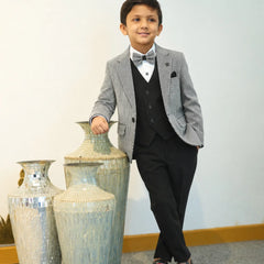 Young boy in a gray blazer and black suit standing next to decorative vases.