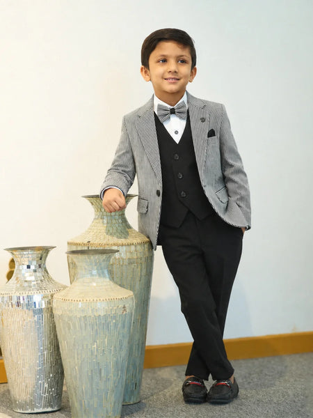 Young boy in a gray blazer and black suit standing next to decorative vases.