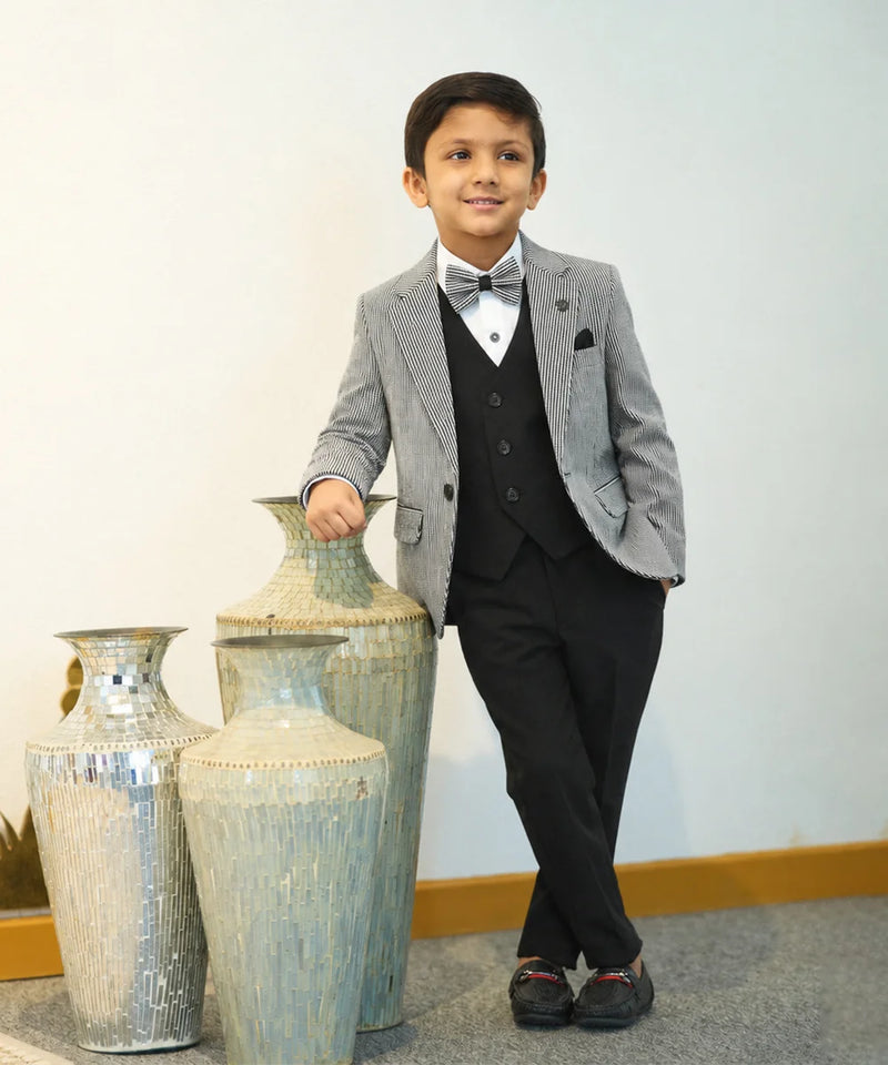 Young boy in a gray blazer and black suit standing next to decorative vases.