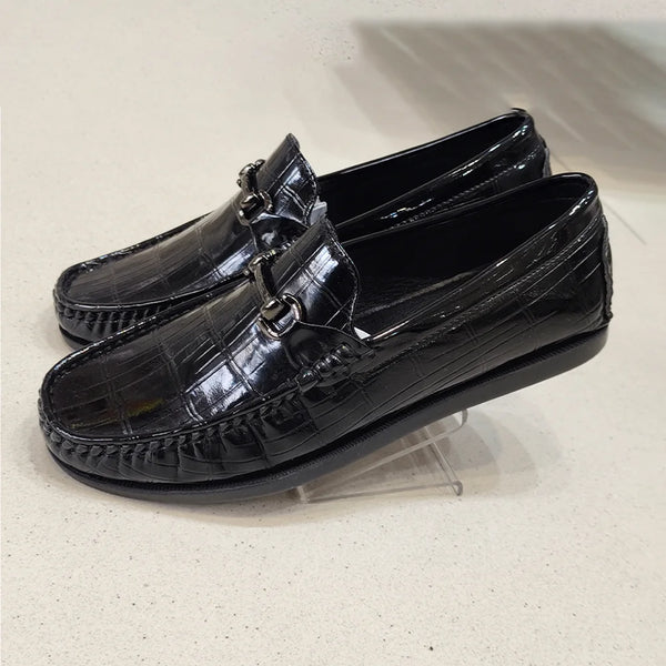Black patent leather loafers on a clear stand against a light background