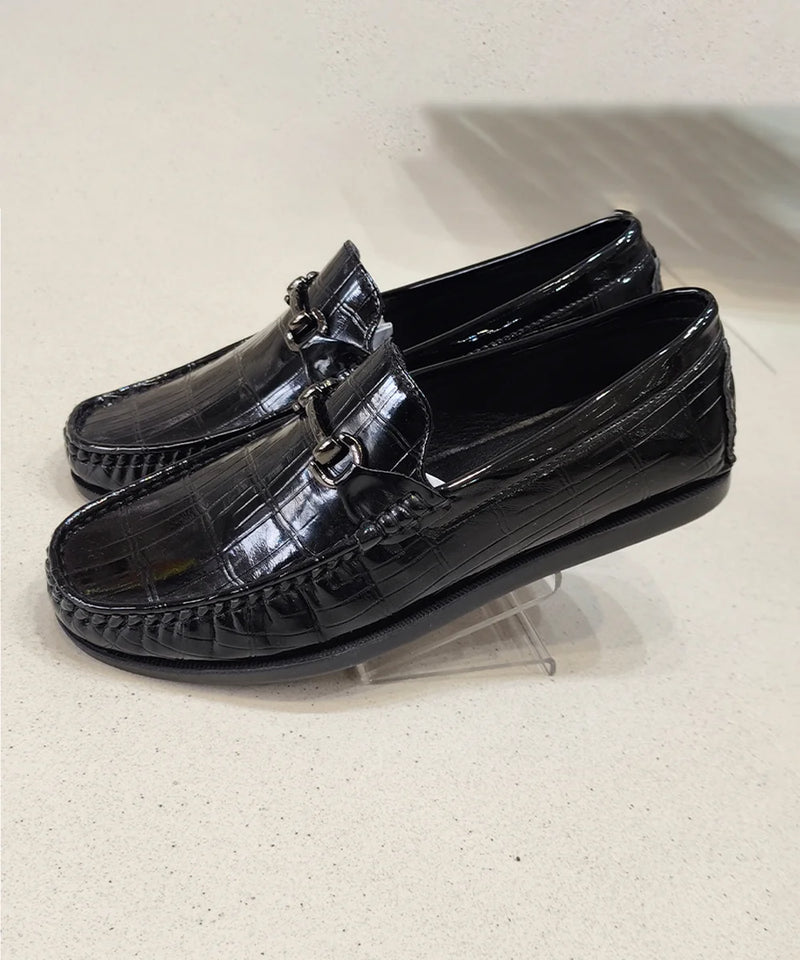 Black patent leather loafers on a clear stand against a light background