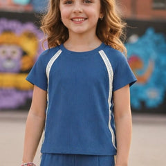 Young girl wearing a blue outfit with white trim in front of colorful murals.
