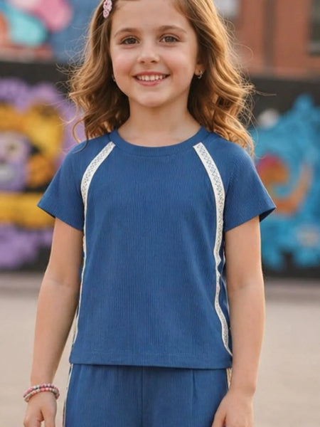 Young girl wearing a blue outfit with white trim in front of colorful murals.