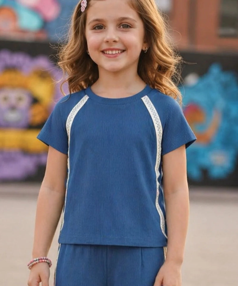 Young girl wearing a blue outfit with white trim in front of colorful murals.