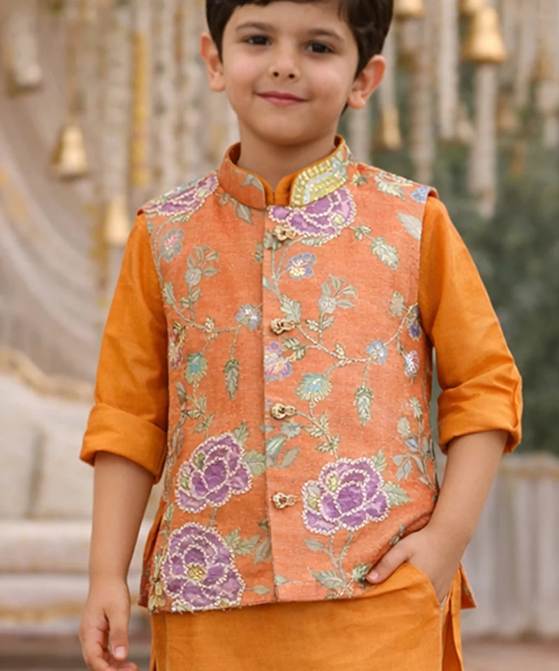 Child wearing an orange embroidered vest over a matching shirt with a blurred decorative background