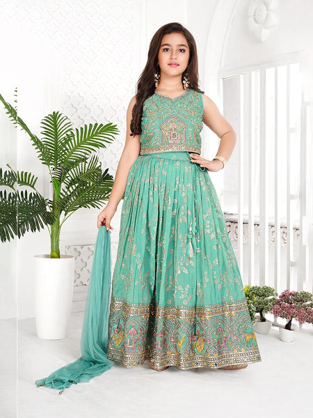 Woman wearing a teal traditional outfit with floral patterns in a bright room.