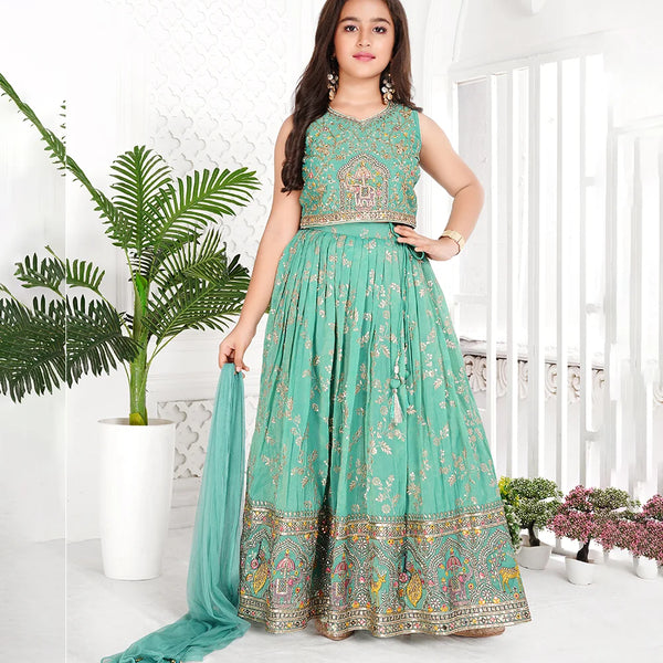 Woman wearing a teal traditional outfit with floral patterns in a bright room.