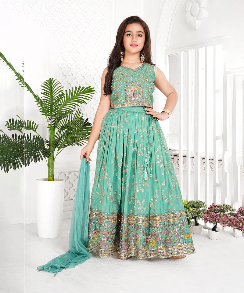 Woman wearing a teal traditional outfit with floral patterns in a bright room.