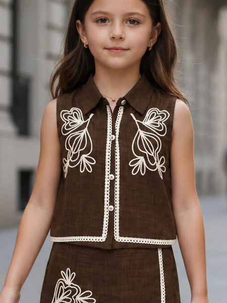 Young girl wearing a brown outfit with white embroidery in an urban setting