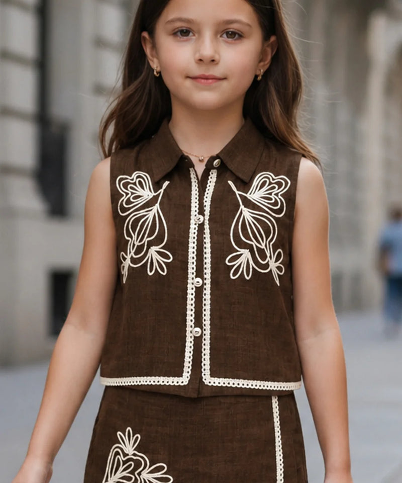 Young girl wearing a brown outfit with white embroidery in an urban setting