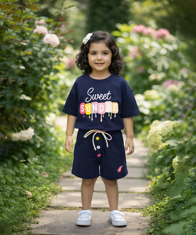 Child wearing a navy blue outfit with colorful text standing in a garden.