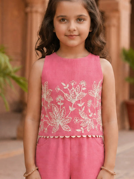 Young girl wearing a pink sleeveless top with white floral embroidery in an outdoor setting.