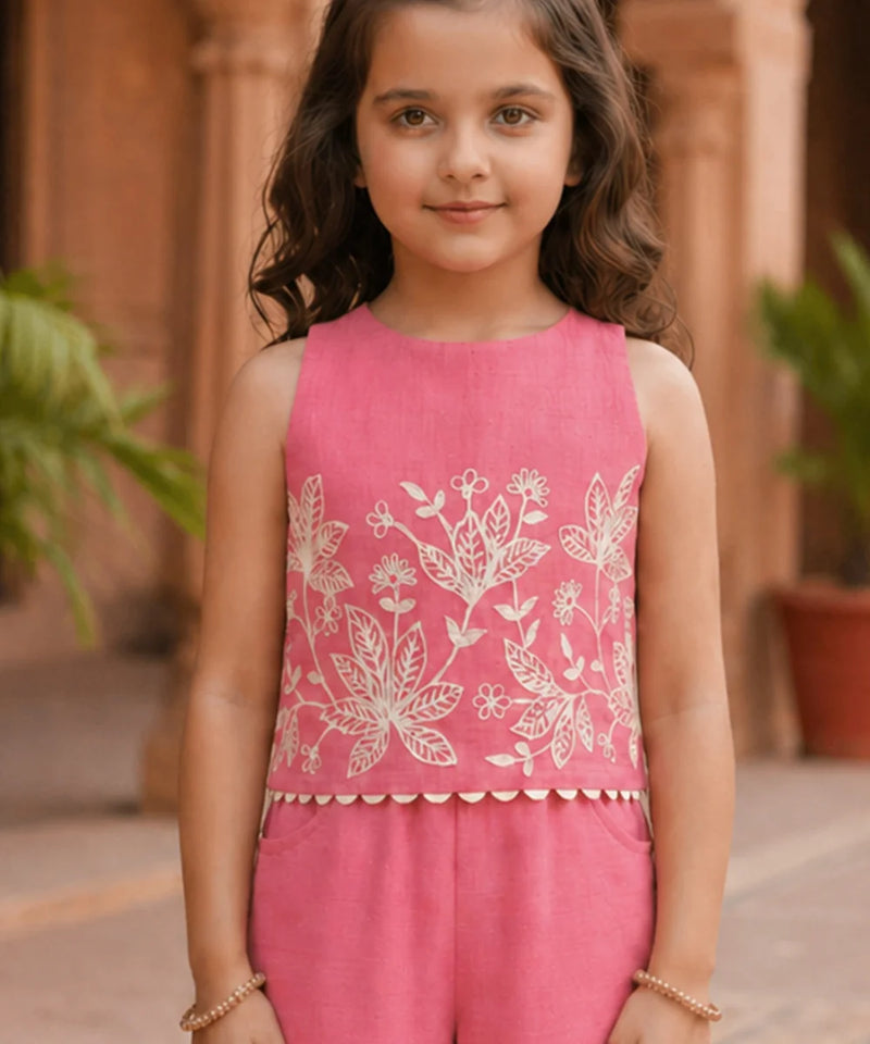 Young girl wearing a pink sleeveless top with white floral embroidery in an outdoor setting.