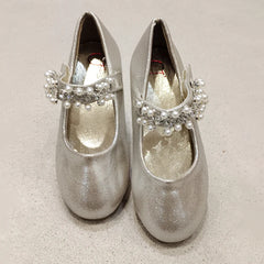 Pair of silver glittery shoes with decorative elements on a beige background