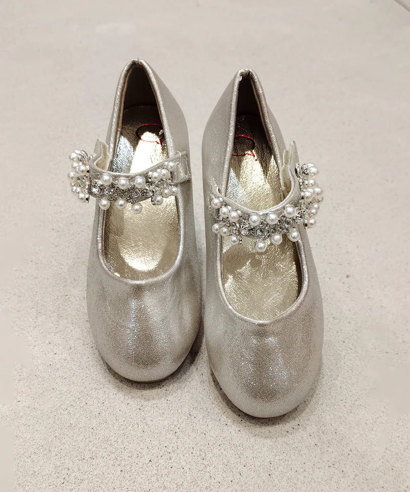 Pair of silver glittery shoes with decorative elements on a beige background