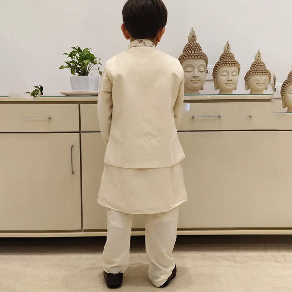 It is a back view of the boy wearing a cream colour kurta pyjama. The back of the jacket is plain.