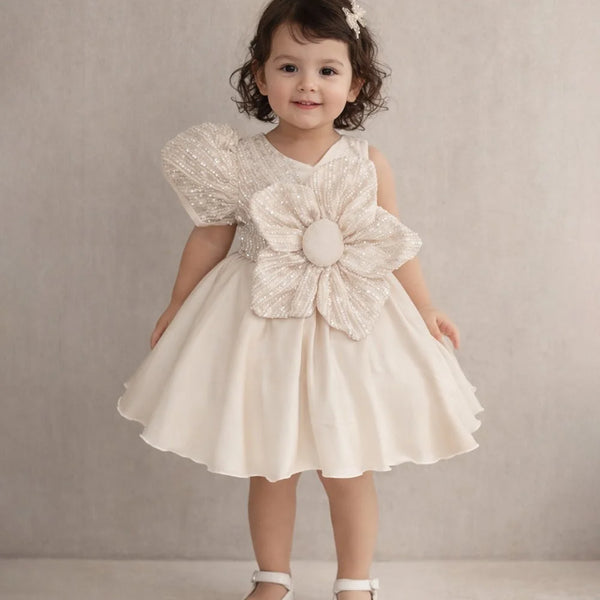Young girl wearing a white dress with a large flower detail against a plain background
