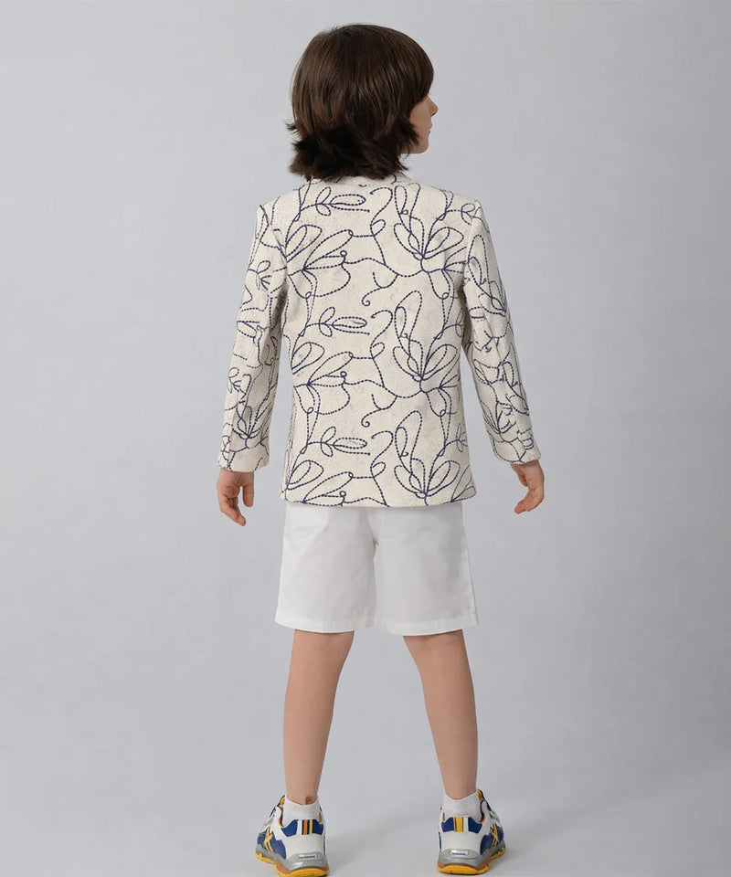 Child wearing a patterned blazer and white shorts on a plain background