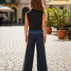 Woman wearing a black sleeveless top and blue wide-leg pants on a cobblestone street.