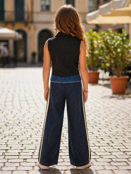 Woman wearing a black sleeveless top and blue wide-leg pants on a cobblestone street.
