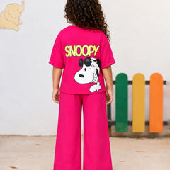A child wearing a bright pink short-sleeve T-shirt with a large Snoopy graphic on the front. The graphic shows Snoopy wearing black sunglasses, a blue jacket, a yellow shirt, and blue jeans, with the word 'SNOOPY' printed below in yellow.