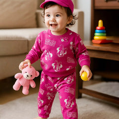 Child wearing a pink Minnie Mouse outfit holding a teddy bear and a ball in a living room.
