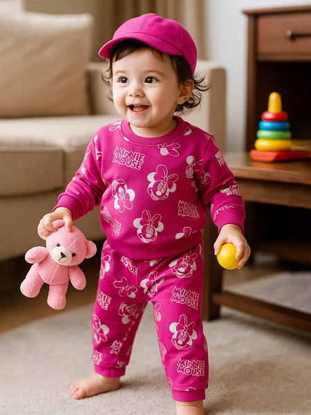 Child wearing a pink Minnie Mouse outfit holding a teddy bear and a ball in a living room.