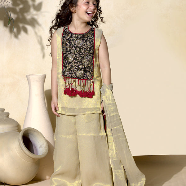 Young girl in traditional outfit with beige top and pants, standing indoors.