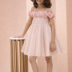 Young girl wearing a pink dress with floral straps against a beige background