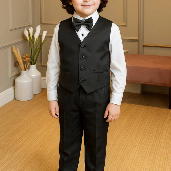 Young boy in a formal black suit standing in a room with light wood flooring and neutral walls.