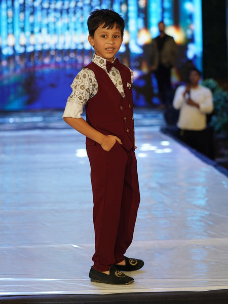 This wedding dress for small boy consists of a maroon Colored waistcoat, matching pants and a self-printed white Coloured shirt. It features a matching bow, a cute broach and a printed pocket square.