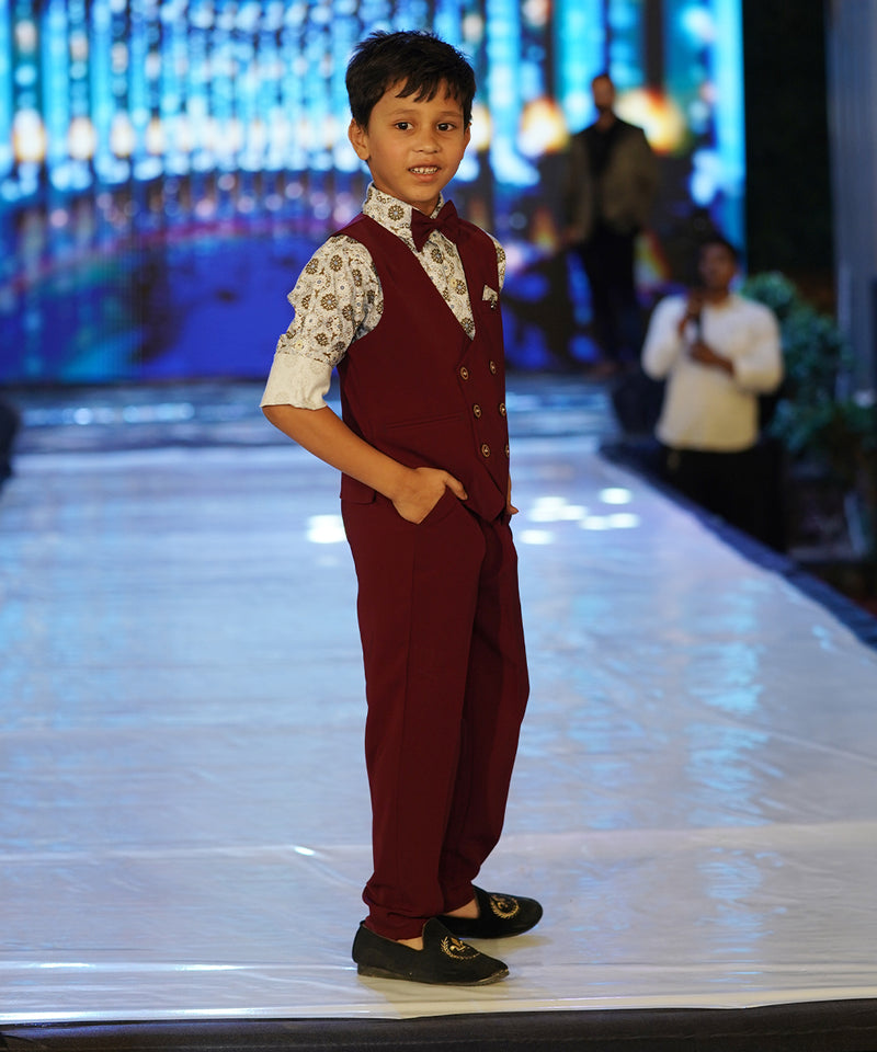 This wedding dress for small boy consists of a maroon Colored waistcoat, matching pants and a self-printed white Coloured shirt. It features a matching bow, a cute broach and a printed pocket square.