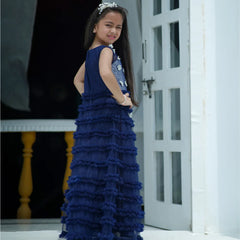 Young girl in a blue ruffled dress standing in a doorway.