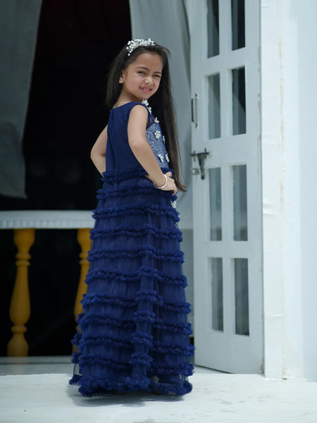 Young girl in a blue ruffled dress standing in a doorway.